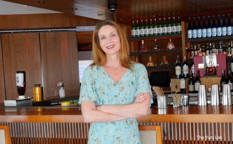 Monica Tindall, de The Yum List, con vestido turquesa frente a la barra de un restaurante; reseñó Tarahumara