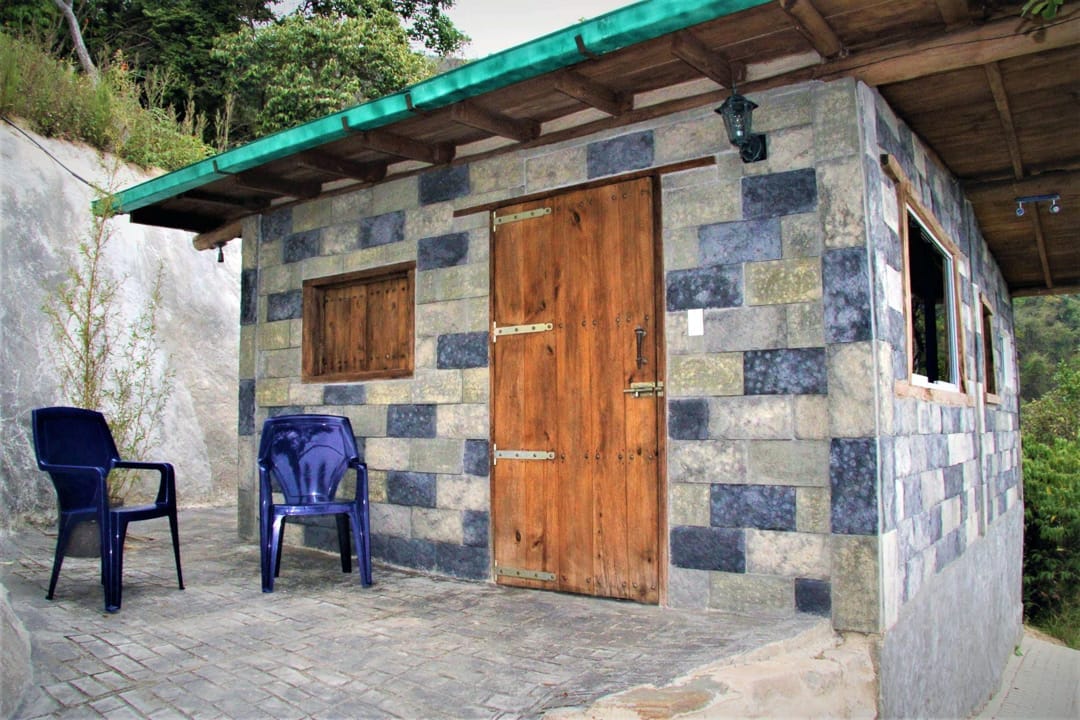 Fachada de piedra de la Cabaña Escondida, con puerta de madera y sillas afuera, entre la vegetación de Galipán