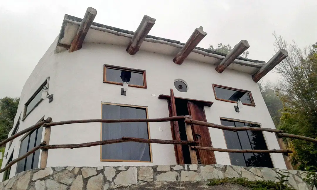 Fachada de dos plantas de la Cabaña Luna, con vigas de madera y base de piedra, entre la neblina de Galipán