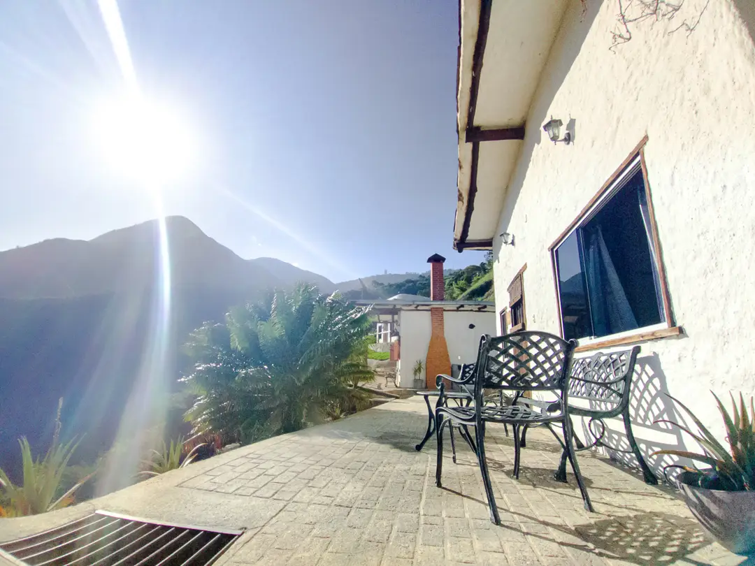 Terraza empedrada de la Cabaña Azahares con sillas de hierro forjado y el sol sobre la montaña de Galipán