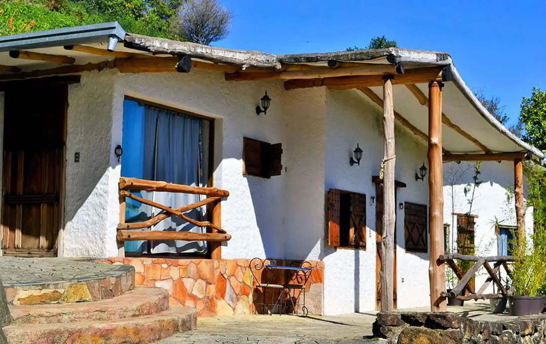 Corredor exterior de la Cabaña Tertulia, con horcones de madera y zócalo de piedra, bajo el cielo de Galipán