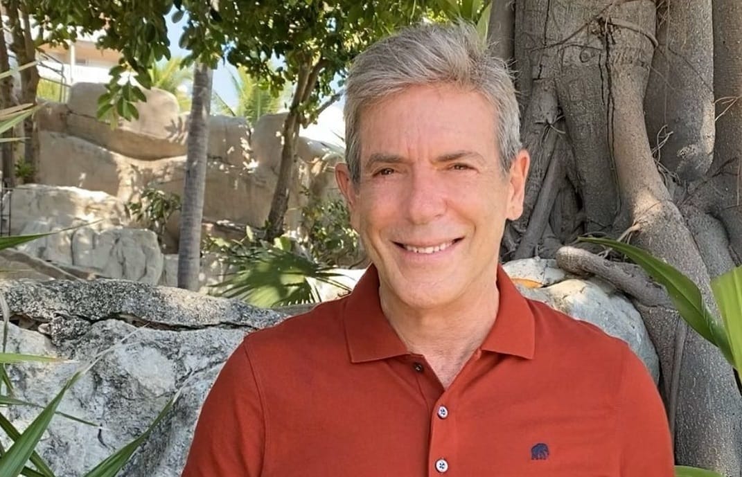 Carlos Mata sonríe al aire libre, con camisa naranja, entre rocas y vegetación; visitó la Posada Tarahumara en Galipán