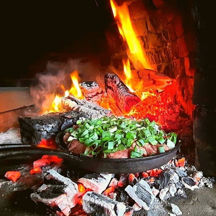 Carne y cebollín en un sartén de hierro sobre las brasas de un fogón de leña en un restaurante de Galipán.