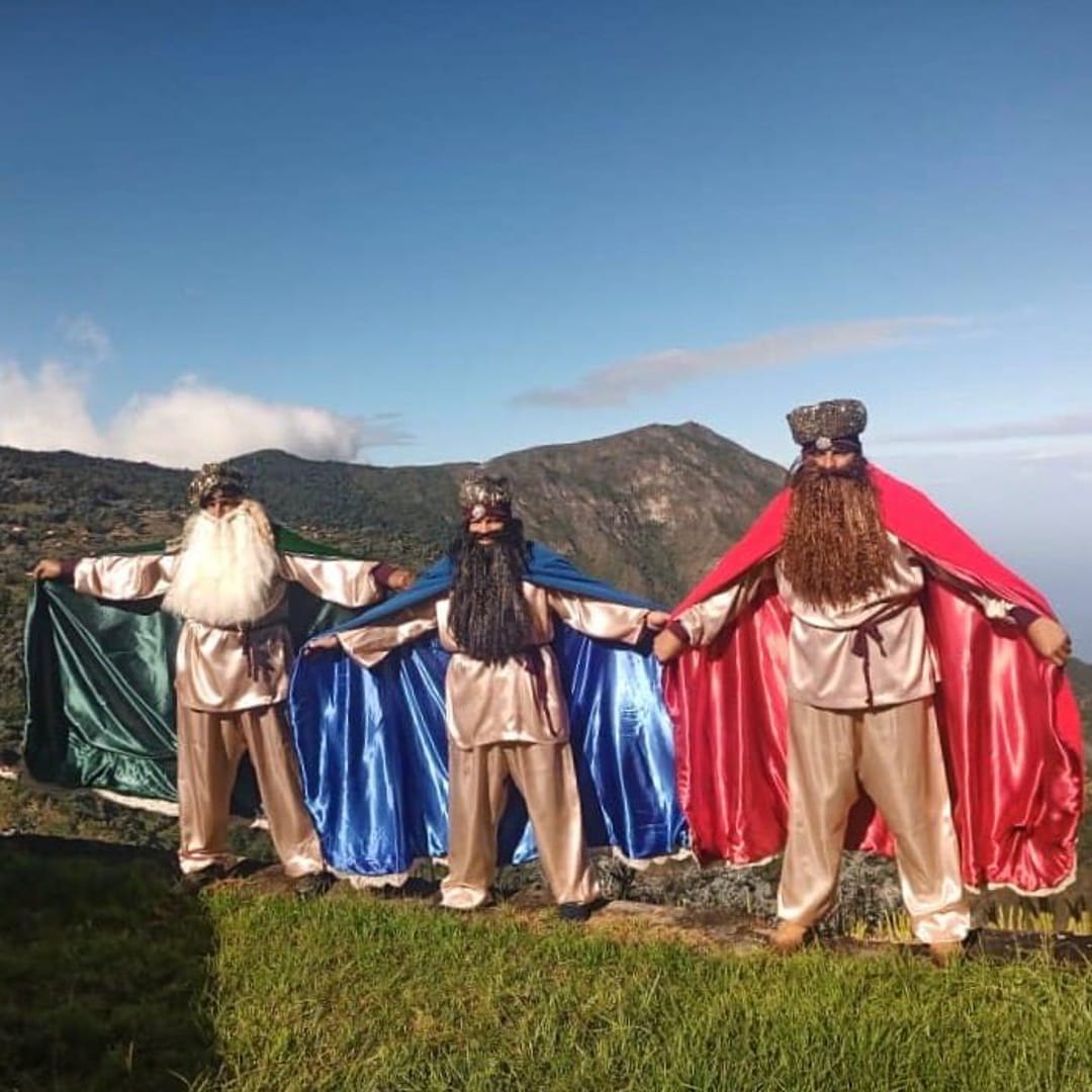 Tres hombres vestidos de Reyes Magos extienden sus capas verde, azul y roja en una loma de Galipán, El Ávila.