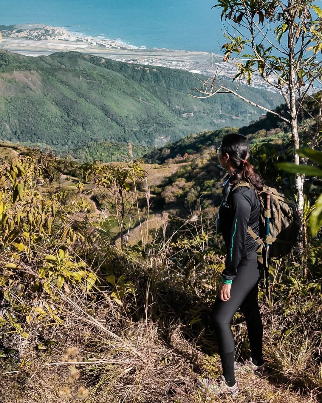 Excursionista con mochila mirando desde un sendero de Galipán hacia las montañas verdes y el litoral de La Guaira