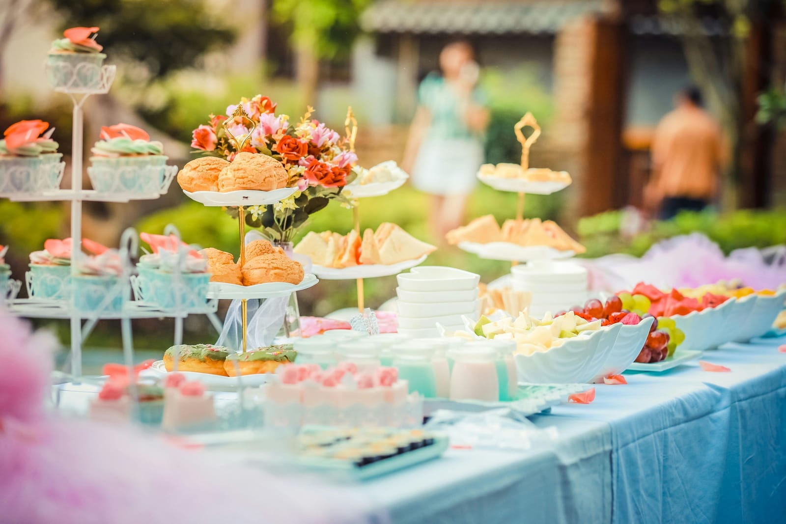 Mesa dulce de baby shower con cupcakes, profiteroles, flores y frutas sobre mantel celeste